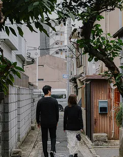 静かな路地裏を、親密な様子で歩く男女の後ろ姿。街の日常に溶け込みながら散策を楽しむ風景。