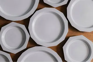 幾何学的なラインが美しい白い八角皿。サイズ違いのプレートが木製の机にランダムに配置されている様子。