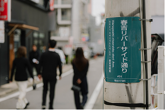 街中を歩く人々と「春吉リバーサイド通り」と書かれた標識の写真