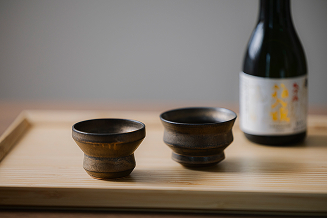 木のトレイに置かれた日本酒の瓶とぐい呑みの写真