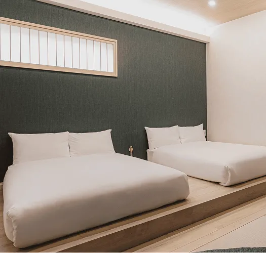 緑のアクセントウォールが印象的な寝室。白いベッドに、足元にはライトが設置されている。