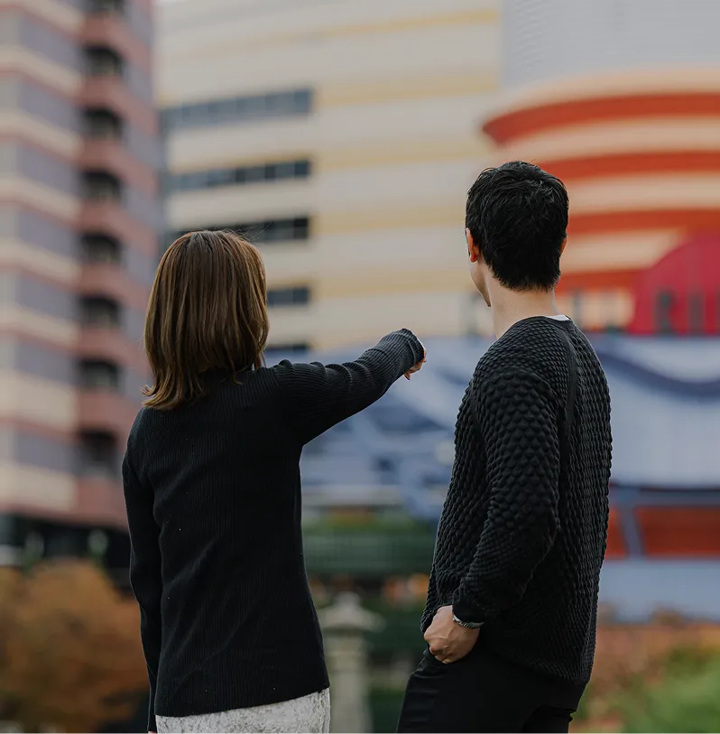 ビルが立ち並ぶ都会の景色を指差して眺める男女の後ろ姿。