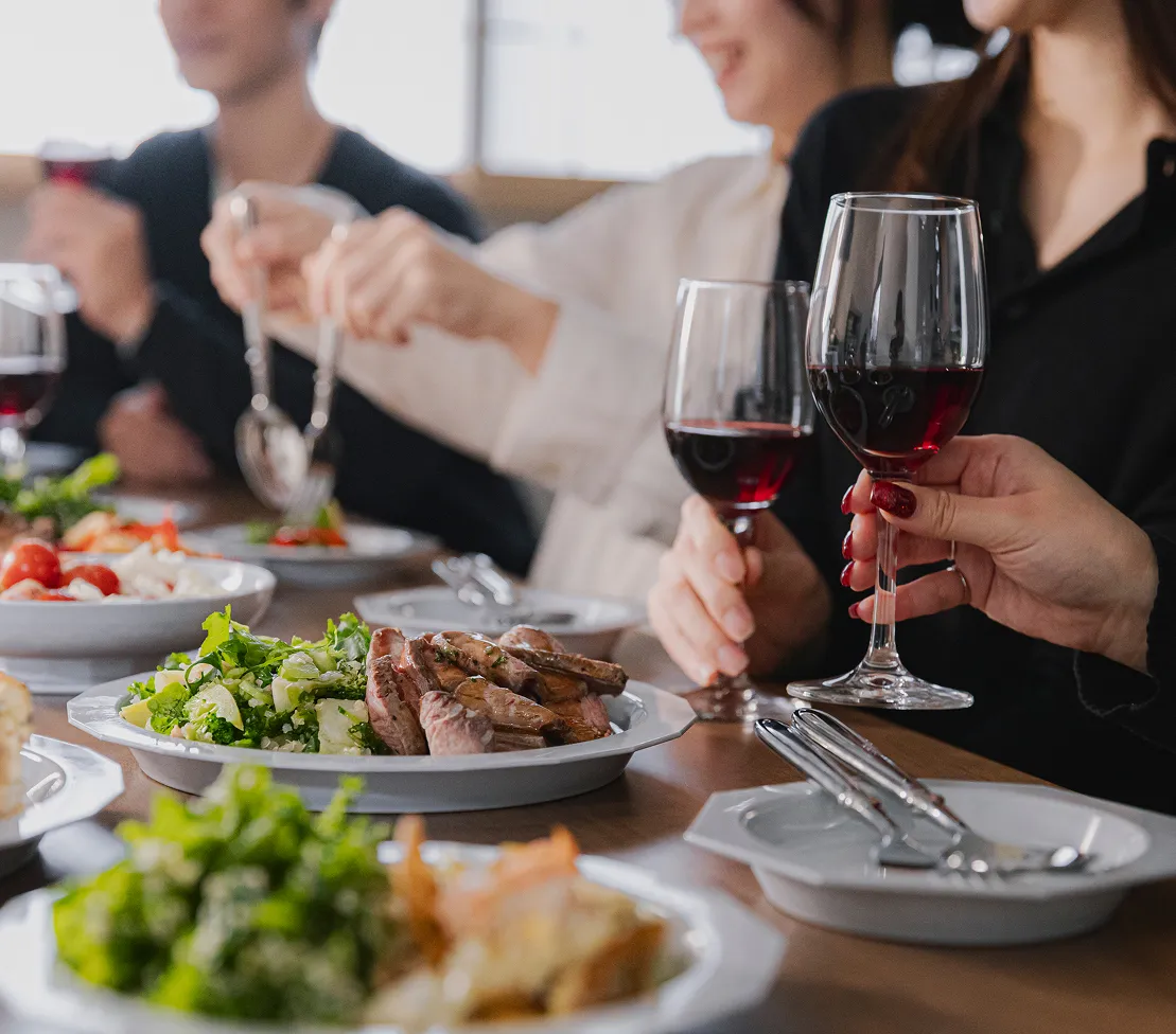 明るいダイニングテーブルを囲み、数名の男女が赤ワインのグラスを手に語らう様子。