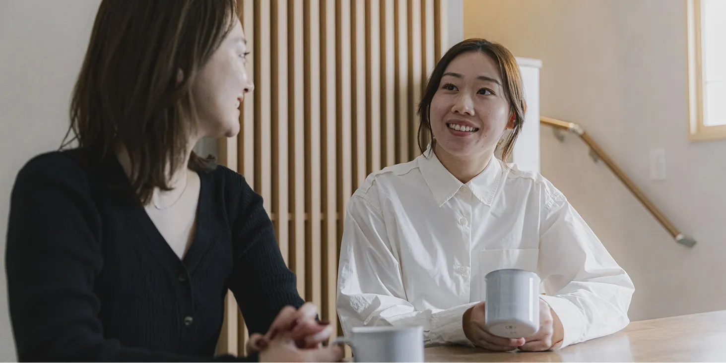 女性二人がリビングでマグカップ片手に会話をしている様子