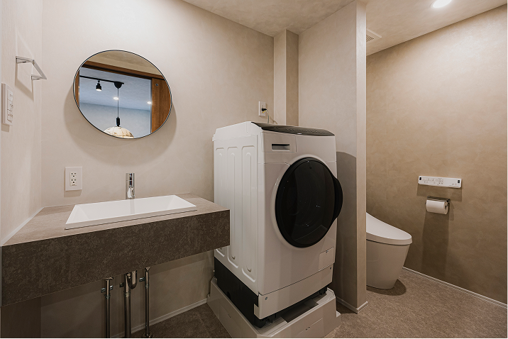 洗面台・ドラム式洗濯機が設置された洗面所、壁を挟んでトイレが設置されている空間