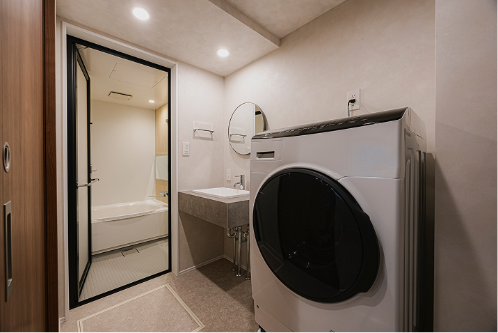 洗面台・ドラム式洗濯機が設置された洗面所、奥には広々とした浴槽がある